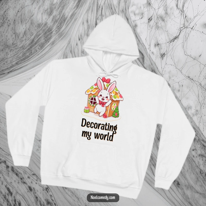 Funny hoodie depicting a bouncing bunny festively decorating a gingerbread house, radiating holiday baking warmth.